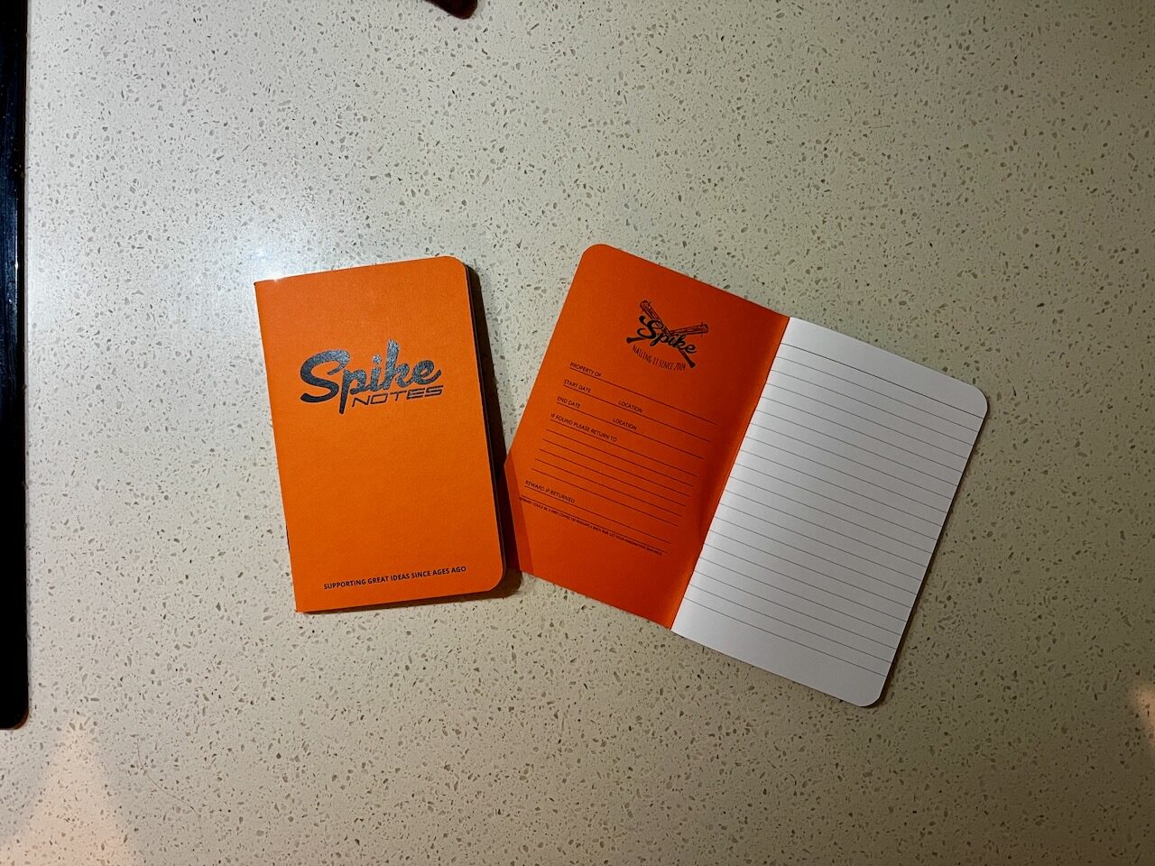 Three orange Spike Notes notebooks, one open to a blank lined page